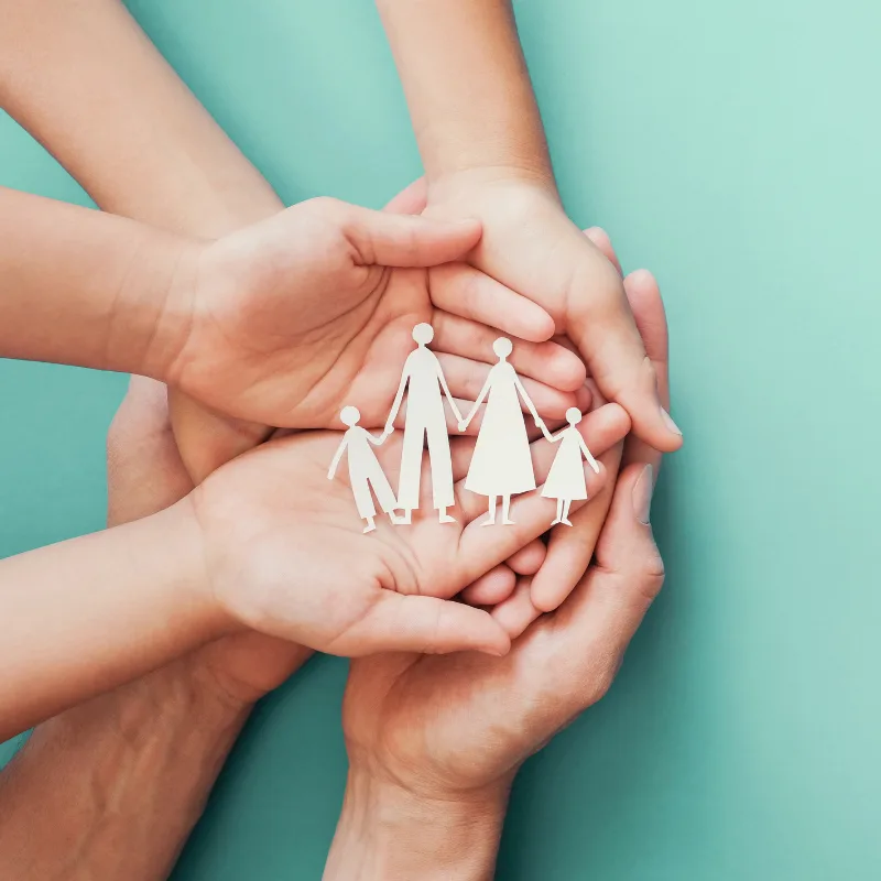 Adult and child hands cupped together, holding a paper cut-out of a family