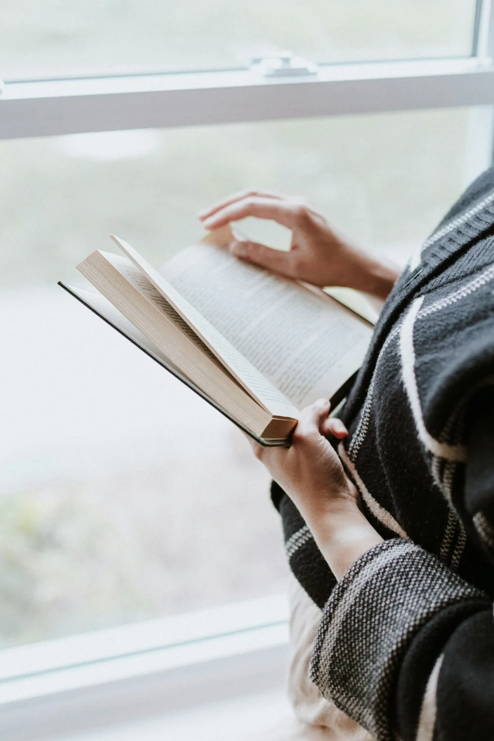 A person sitting by a bright window, reading a book